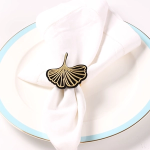 Elegant black and gold ginkgo leaf napkin ring placed on white fabric in a ceramic plate