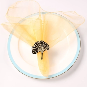 Macro detail of golden ginkgo leaf napkin ring with black inlay on yellow napkin