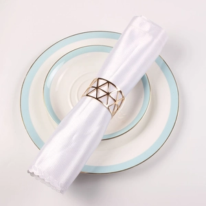 Rose gold hollow triangle napkin ring on white satin cloth with elegant dinnerware