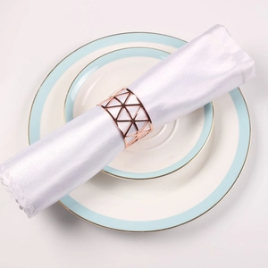 Detail shot of hollow geometric triangle napkin ring in rose gold on white fabric