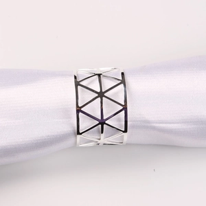Detail of silver X-shaped metal napkin ring with modern geometric hollow design on white fabric