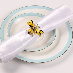 Detailed close-up of a bee-shaped napkin ring with gold enamel and crystals on a white napkin