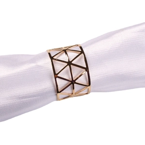 Modern gold metal X-shaped napkin ring with geometric cutout on white napkin