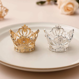 Golden and silver crown napkin rings with rhinestones on a beige ceramic plate