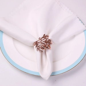 Macro detail of rose gold hazelnut napkin ring with acorn and leaf relief on white cloth