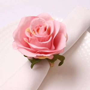 Pink artificial rose napkin ring with green leaves on white napkin and ceramic plate