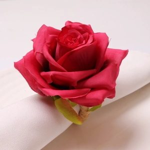 Detail of a red faux rose napkin ring with green leaves on white linen for wedding decor