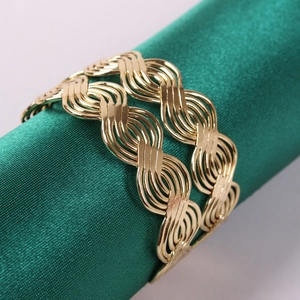 Close-up of polished gold napkin ring with wave texture on dark green satin fabric