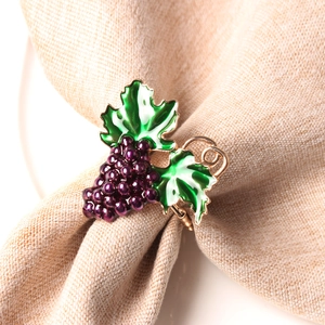 Macro detail of purple grape napkin ring with green enamel leaves on a linen cloth