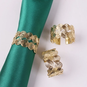 Close-up of golden woven metal napkin ring with wave design on green fabric