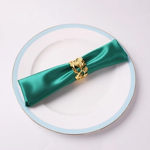 Close-up of gold maple leaf napkin ring with hollowed detail on a dark green satin cloth