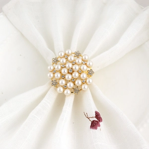 Elegant gold napkin ring with white pearls and rhinestones on a white linen napkin
