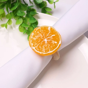 Close-up of artificial orange slice napkin ring on a white plate with green leaves decoration