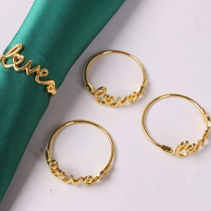 Detailed view of four golden Love letter napkin rings on green silk and marble surface