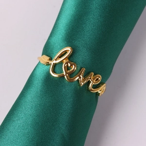 Detail of golden Love letter napkin ring with heart design on green silk fabric