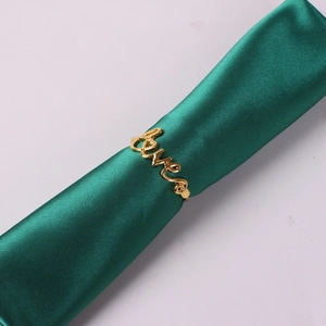 Detail of gold Love napkin ring with polished metal finish on green satin ribbon