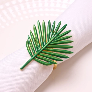 Detailed view of a green palm leaf napkin ring with gold metal finish on white fabric