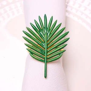 Green enamel palm leaf napkin ring with golden metallic edges on a white cloth