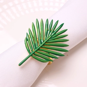 Close-up of golden palm leaf napkin ring with green enamel finish on a white napkin