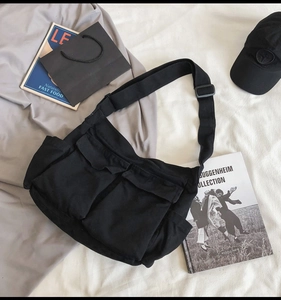 Detail view of a black canvas messenger bag with dual front utility pockets and wide strap