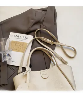 Detail der cremefarbenen Ledertasche mit Markenlogo und Goldbuckle auf braunem Blazer