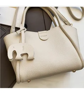 Detail der cremefarbenen Tasche mit Litschi-Struktur, Elefanten-Anhänger und Metallfüßen