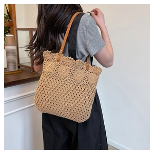 Detail of hollow floral crochet pattern and brown leather handle on a woven tote bag