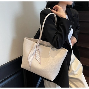 Detail of off-white lychee leather tote bag with elegant silk scarf on the handle
