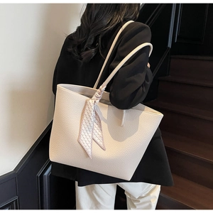 Detail of a large off-white leather tote bag with a decorative silk scarf on the handle