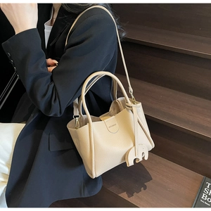 Detailansicht der beigen Ledertasche mit Elefantenanhänger auf einer Holztreppe