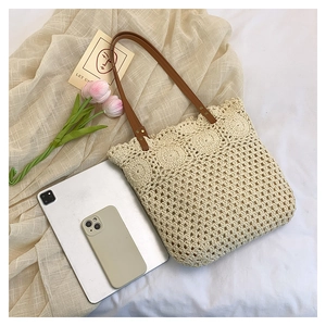 Close-up of beige crochet tote bag with brown leather handles and metal rivets