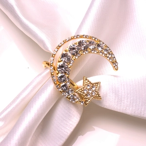 Detailed view of a gold star and moon napkin ring with rhinestones on white satin