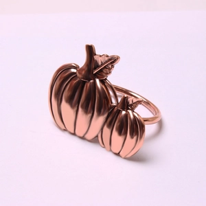 Polished rose gold pumpkin napkin ring featuring detailed leaves on a light pink surface