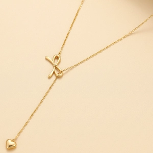 Détail du collier en Y doré avec un nœud papillon et un pendentif cœur suspendu