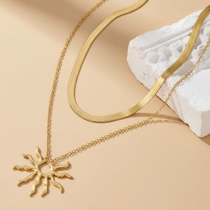 Detail of gold double-layered necklace featuring flat snake chain and sunburst pendant