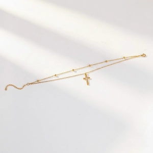 Detail of 18K gold double-layer anklet with cross pendant and small gold beads