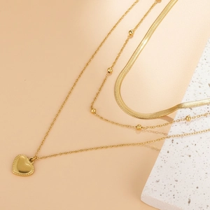 Detail of layered gold snake chain necklace with a heart pendant on textured stone