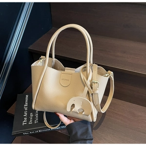 Detailansicht der beigen Handtasche aus genarbtem Leder mit Elefantenanhänger auf Holzstufen
