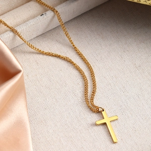 Close-up of a minimalist gold cross pendant necklace on elegant satin and textured cloth