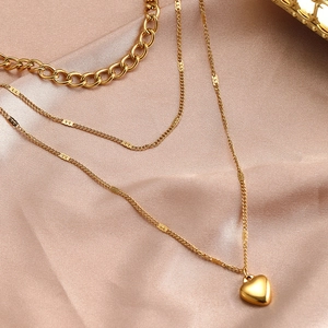 Detailansicht mehrlagiger 18K Gold-Edelstahlketten mit Herzanhänger auf rosa Satinstoff