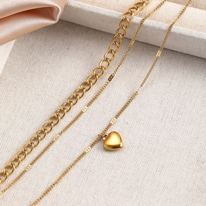 Nahaufnahme der goldenen Lagenkette mit Gliederkette und Herzanhänger auf Stoff
