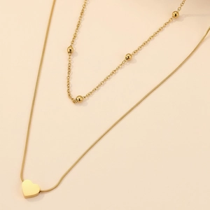 Détail d'un collier double épaisseur doré avec pendentif cœur et chaîne à billes fine