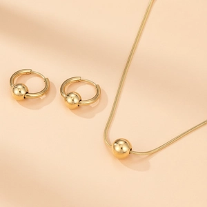 Vue détaillée des boucles d'oreilles dorées et du collier assorti sur fond rose poudré