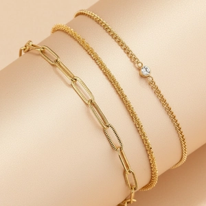 Detail of gold paperclip, woven, and zircon stone chain bracelet set on display