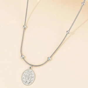 Silver bead snake chain necklace with an oval embossed pendant on a beige background