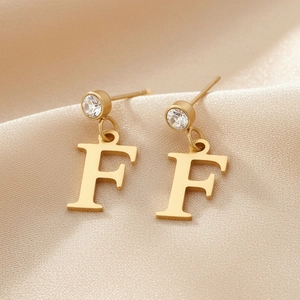 Vue détaillée des boucles d'oreilles lettre F en or 18K avec zircon sur soie champagne