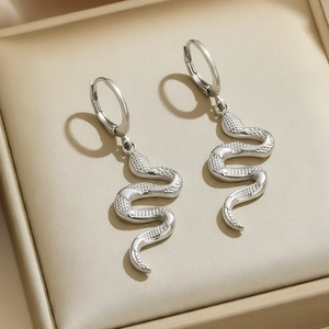 Silver polished stainless steel hoop earrings featuring detailed snake pendants on beige