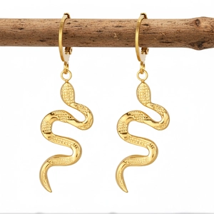 Detailed view of gold snake hoop earrings hanging on a natural wooden branch