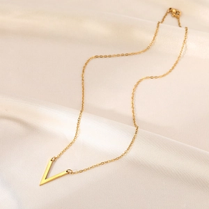 Détail d'un collier avec pendentif en V doré posé sur un tissu de soie blanche