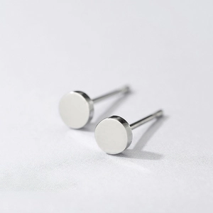 Close-up of polished silver stainless steel round stud earrings on white textured card